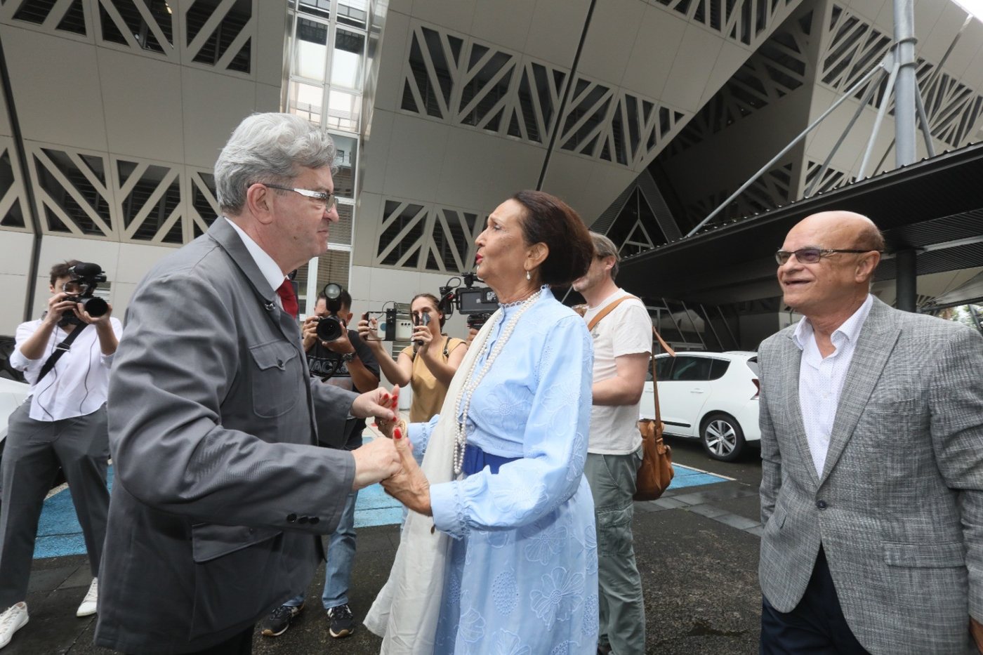 Huguette Bello accueille Jean-Luc Mélenchon devant l’hôtel de Région, accolade et poignée de main.